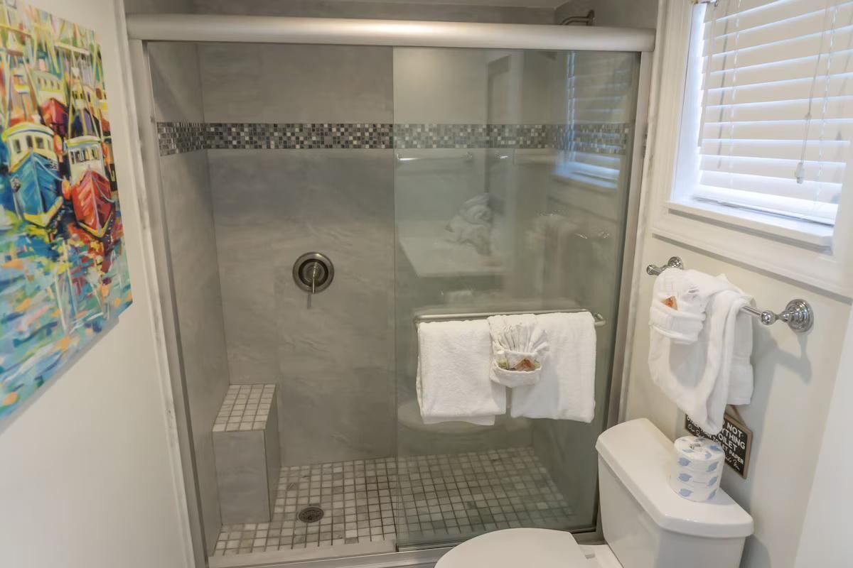 A bathroom with a glass-enclosed shower, a toilet with a paper towel holder, and a towel rack.