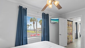 Une chambre d’hôtel avec un lit, un ventilateur de plafond, un téléviseur fixé au mur et une vue sur les palmiers par la fenêtre.