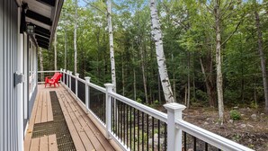 A wooden deck with a white railing, two red Adirondack chairs, and a forested backdrop.