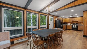 A spacious kitchen with wooden cabinets, a large dining table, and a view of the forest through large windows.