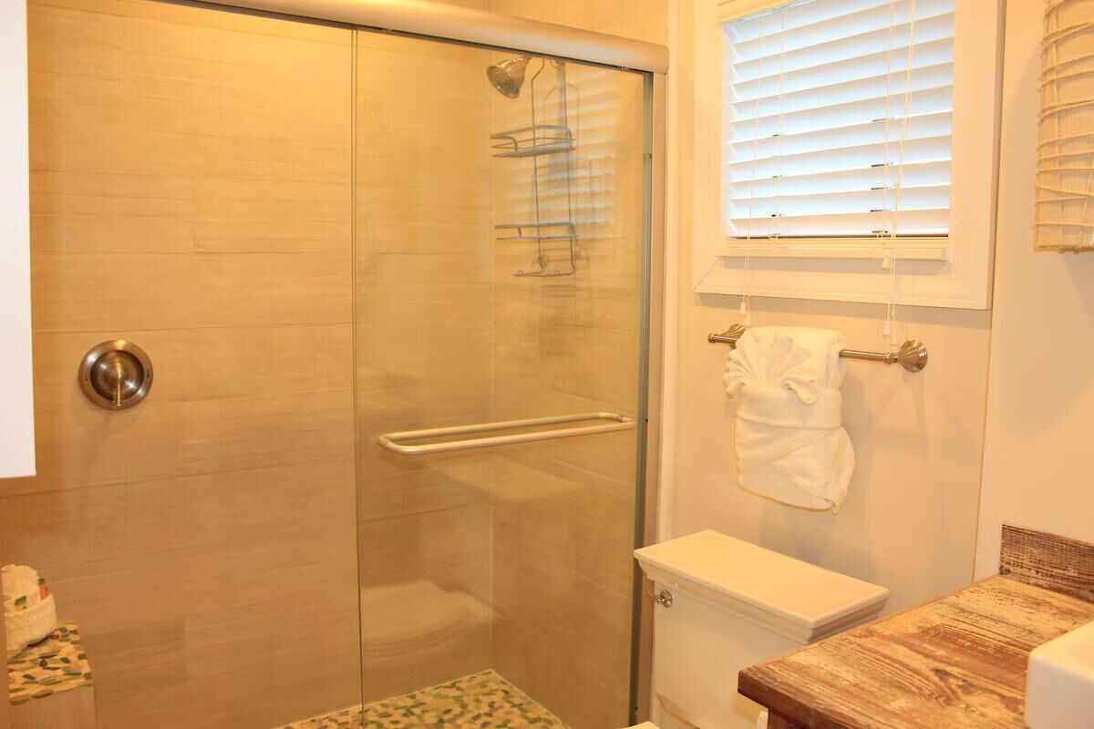 A bathroom with a glass shower enclosure, a toilet, and a sink with a wooden countertop.