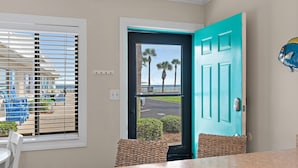 Una habitación con vista a la playa, una puerta color turquesa y una silla de mimbre.