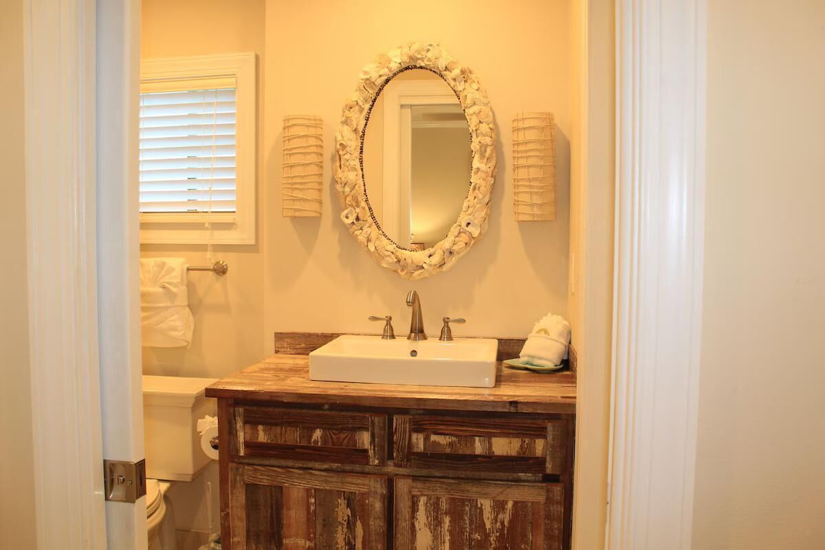 A bathroom with a wooden vanity, a white sink, and a mirror with a floral frame.