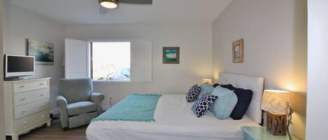 Une chambre à coucher comprenant un lit, une chaise, une commode, un téléviseur et un ventilateur de plafond.