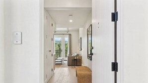 A hallway leading to a living area with a sofa, a small table, and a view of greenery outside.