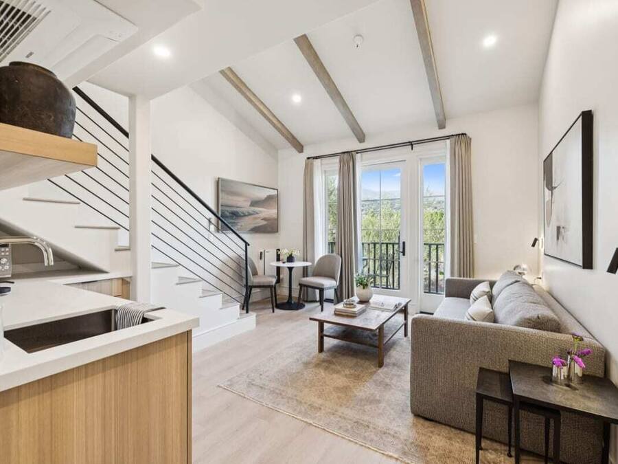 A modern apartment with a kitchen, dining area, and living room. It features a staircase, a balcony with a view, and a large window.