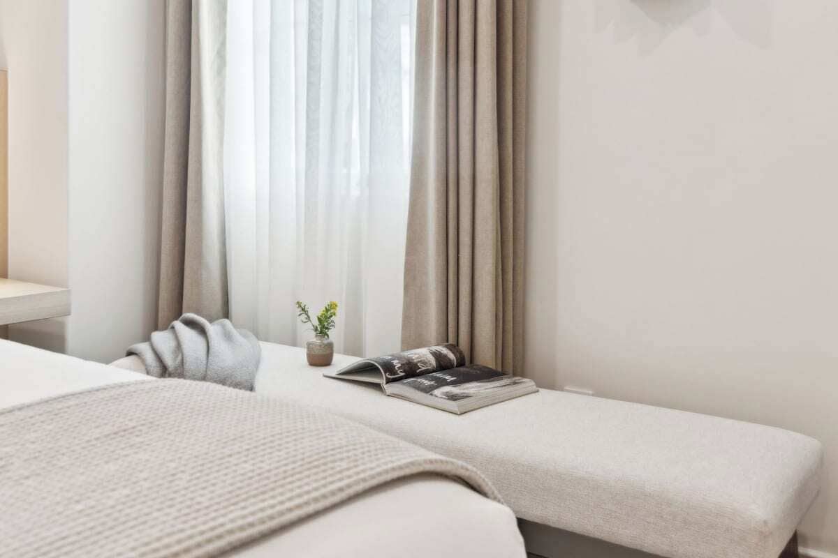 A hotel room with two beds, a bedside table, a window with curtains, and a small potted plant.