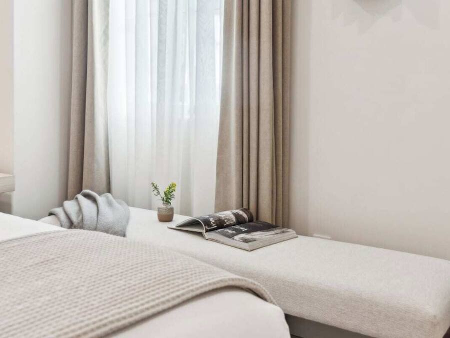 A hotel room with two beds, a bedside table, a window with curtains, and a small potted plant.