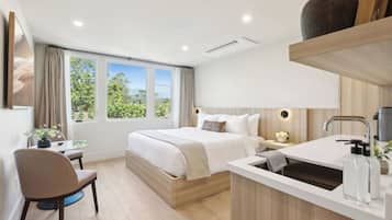 A modern bedroom with a large bed, bedside tables, a desk, and a window with a view of greenery.