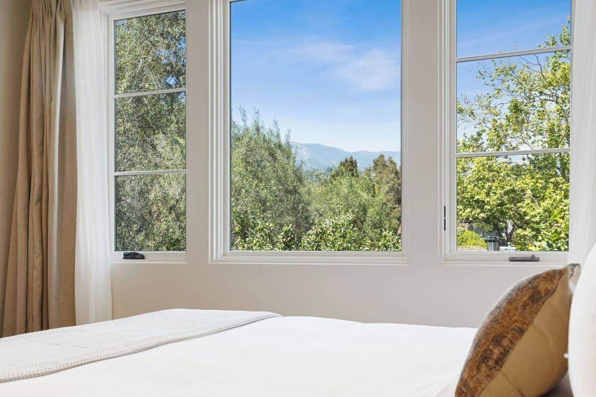 A bedroom with a large window offering a view of a forest and mountains.