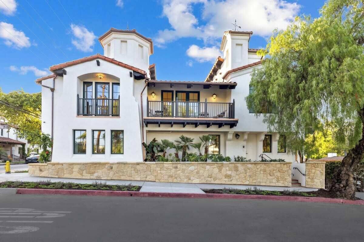 A two-story house with a stone facade, a balcony with black railings, and a clear blue sky.