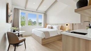 A modern bedroom with a large window, a bedside table, a chair, and a built-in kitchen area.