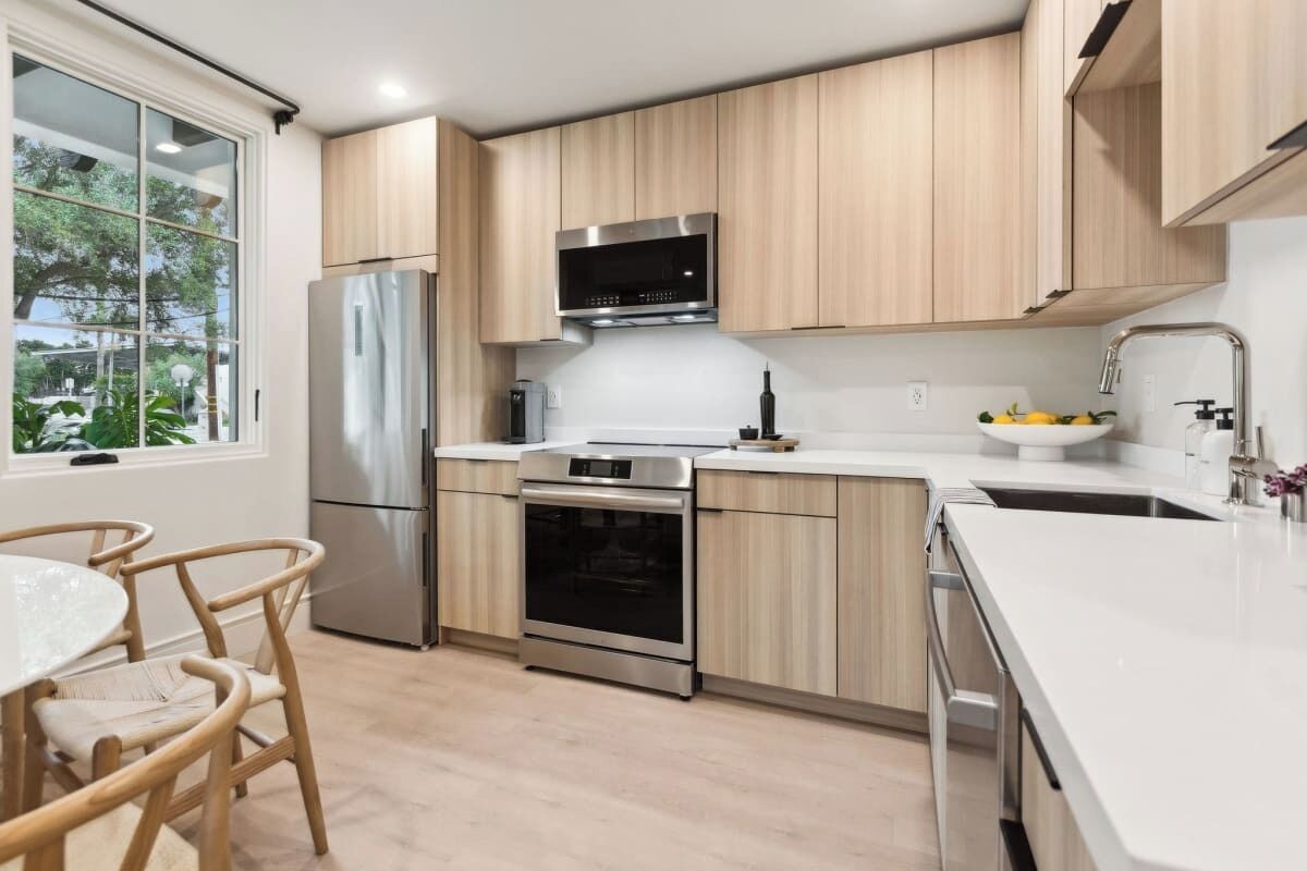 A modern kitchen with stainless steel appliances, wooden cabinets, and a white countertop.