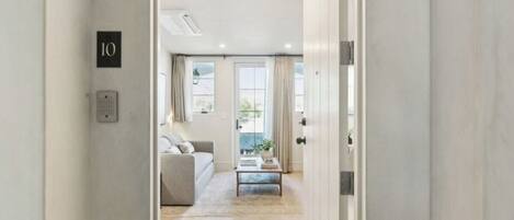 A hallway leading to a living area with a sofa, a coffee table, and a view of the outside.