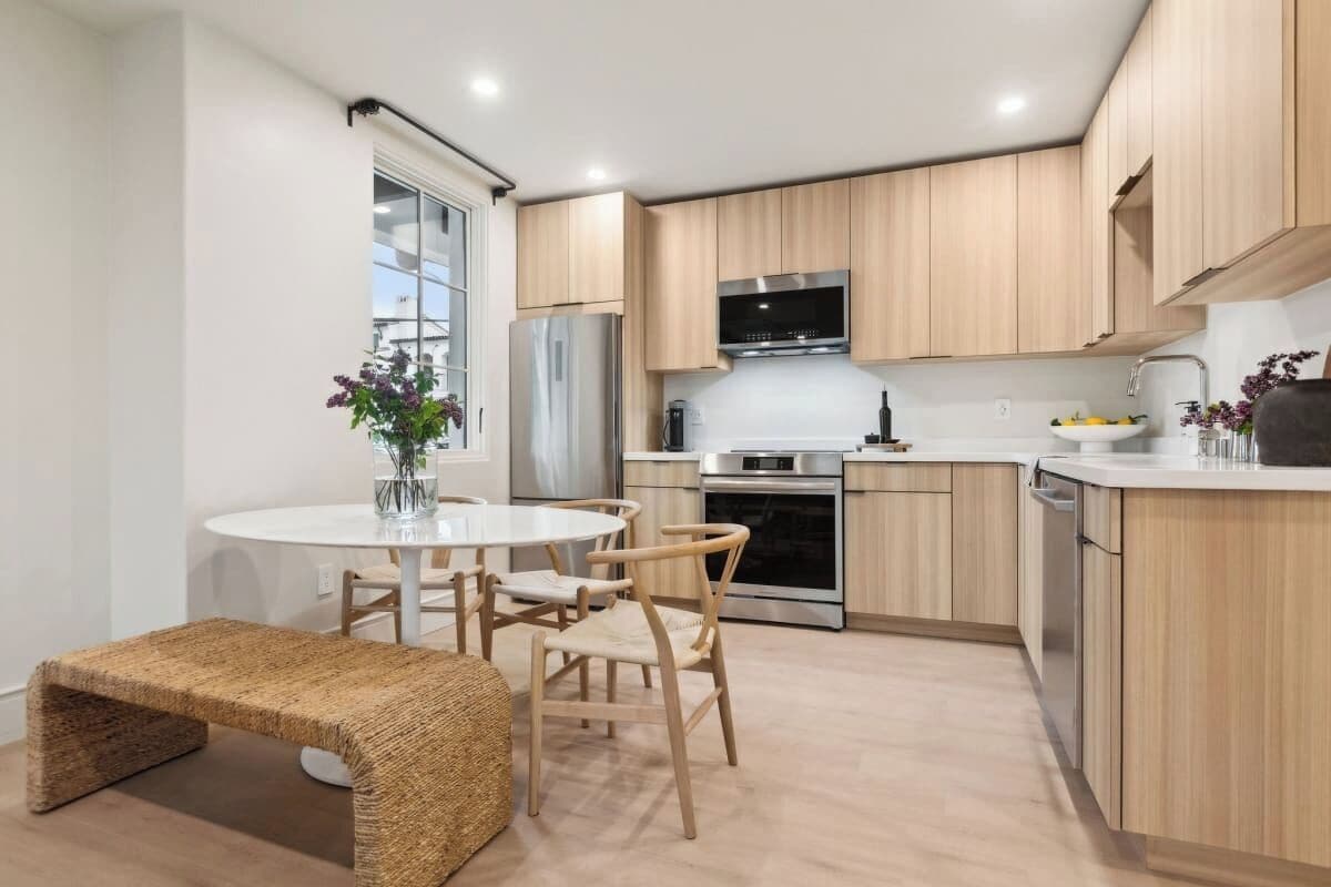 A modern kitchen with wooden cabinets, stainless steel appliances, and a round dining table with chairs.