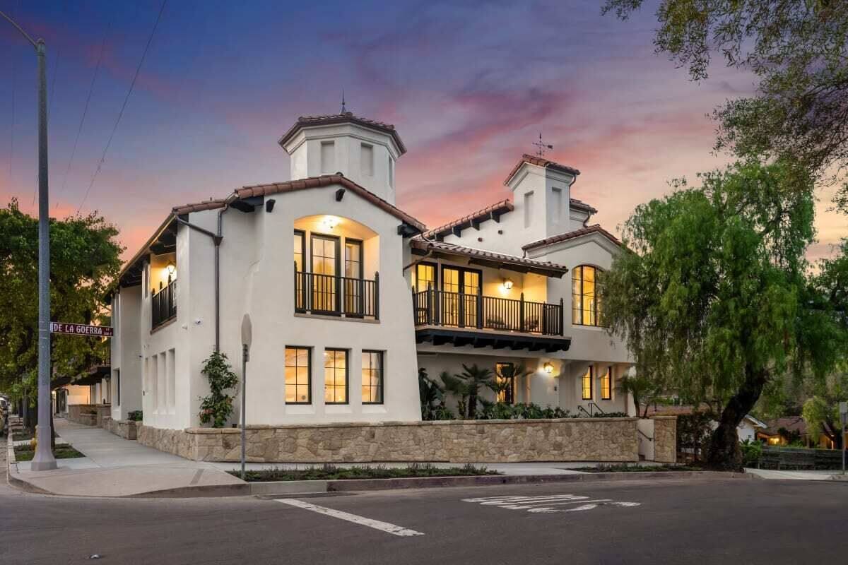A two-story house with a stone foundation, multiple windows, and a balcony.