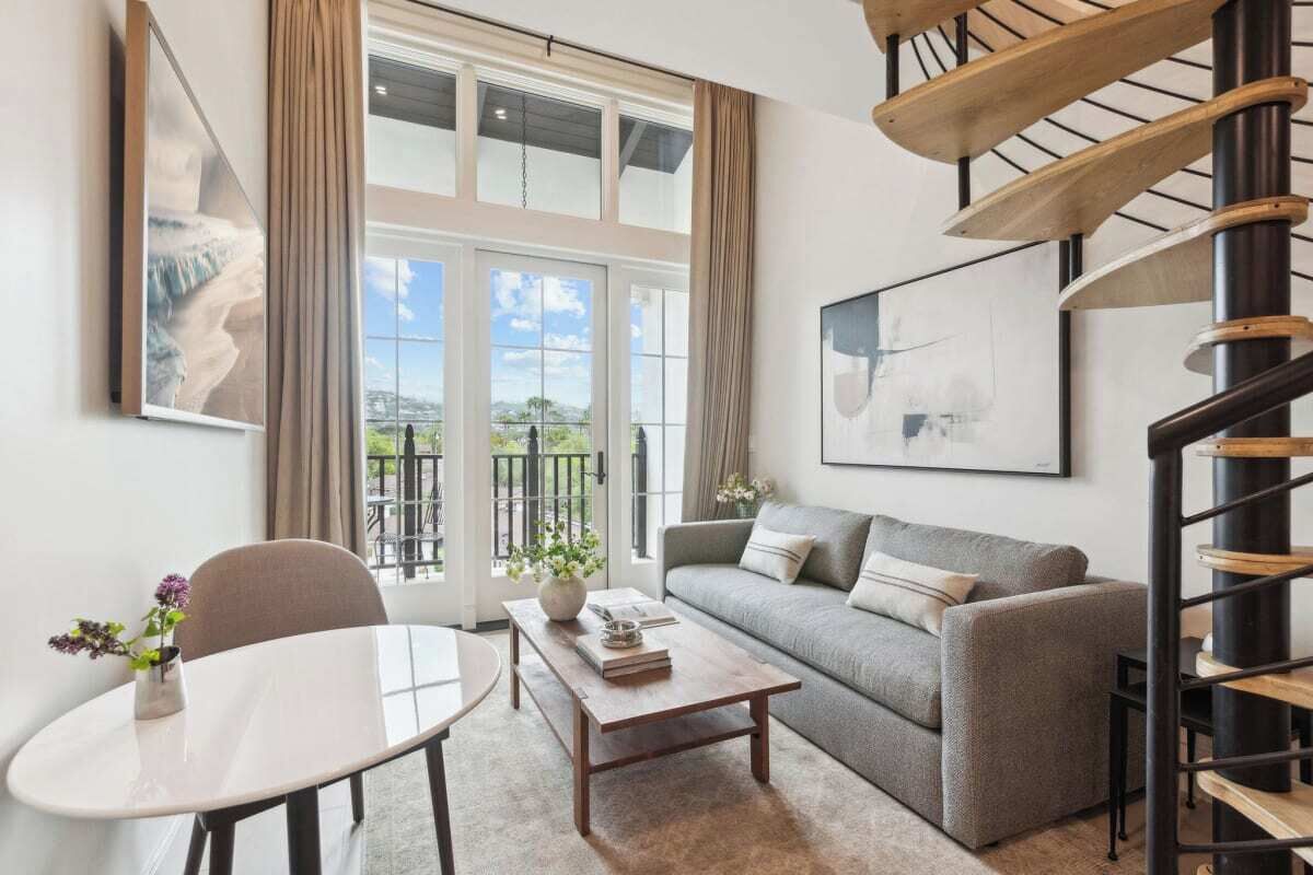 Un salon moderne avec un canapé, une table basse et une table à manger. Un escalier en colimaçon se trouve sur la droite.