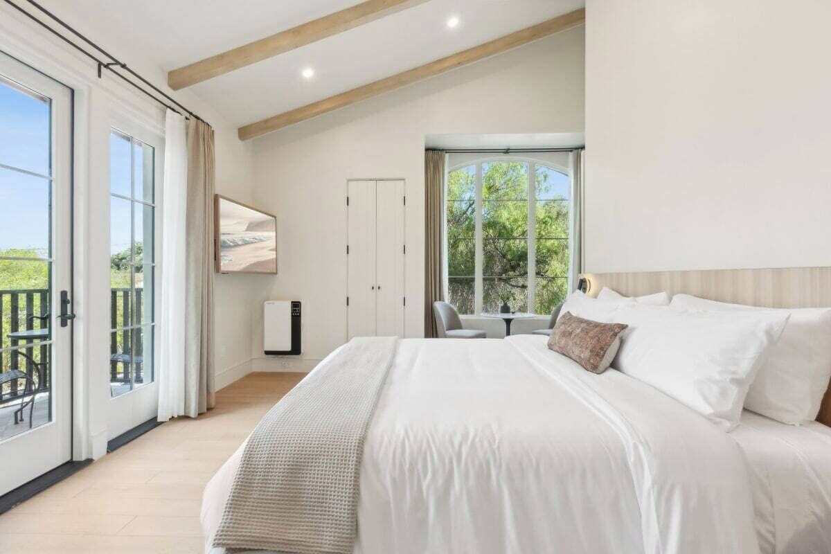 A bedroom with a large bed, a desk, and a view of the outdoors.