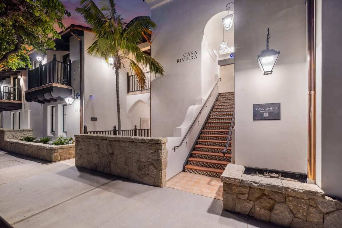 A hotel entrance with a staircase, stone walls, and a palm tree.