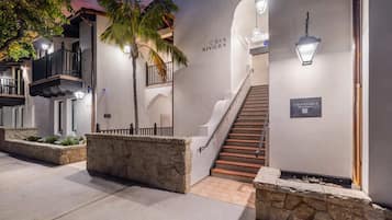 A hotel entrance with a staircase, stone walls, and a palm tree.