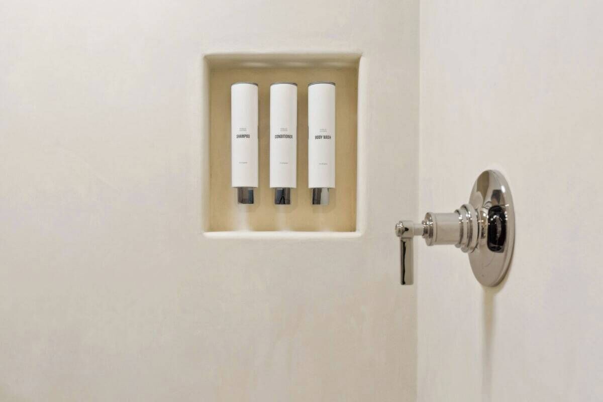 A bathroom with a built-in shelf holding three toiletries: shampoo, conditioner, and body wash.