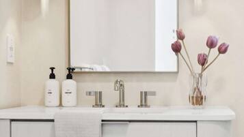 A bathroom vanity with a mirror, two bottles of lotion, a faucet, and a vase with flowers.