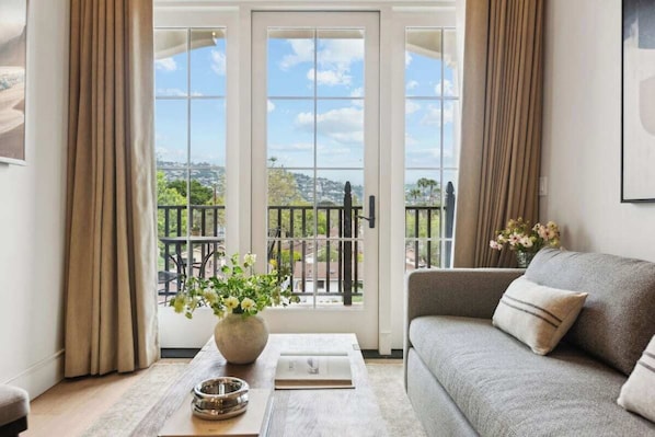 A living room with a sofa, a coffee table, a vase with flowers, and a view through glass doors to the outside.