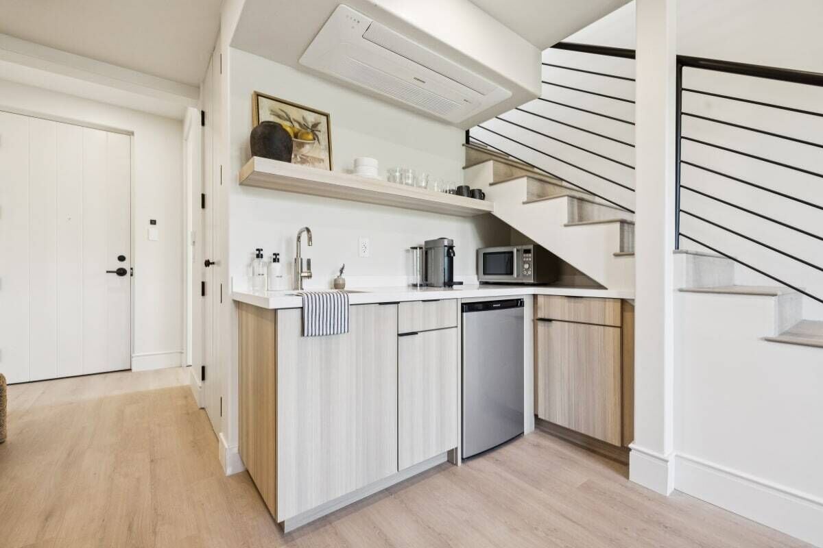 Een moderne keuken met een vaatwasser, magnetron en koffieapparaat. Een trap bevindt zich rechts.