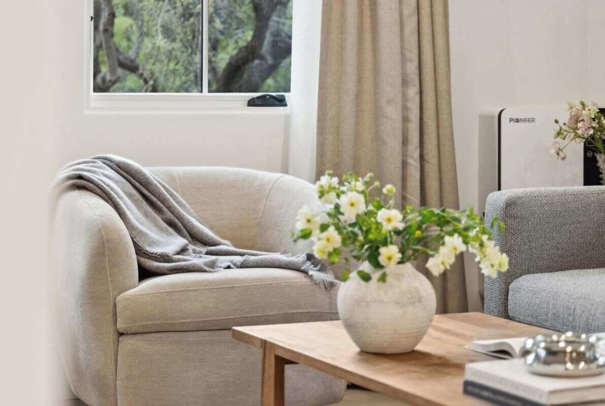En stue med en beige sofa, et træ sofabord med en vase med blomster, og en Pioneer hvidevare i baggrunden.
