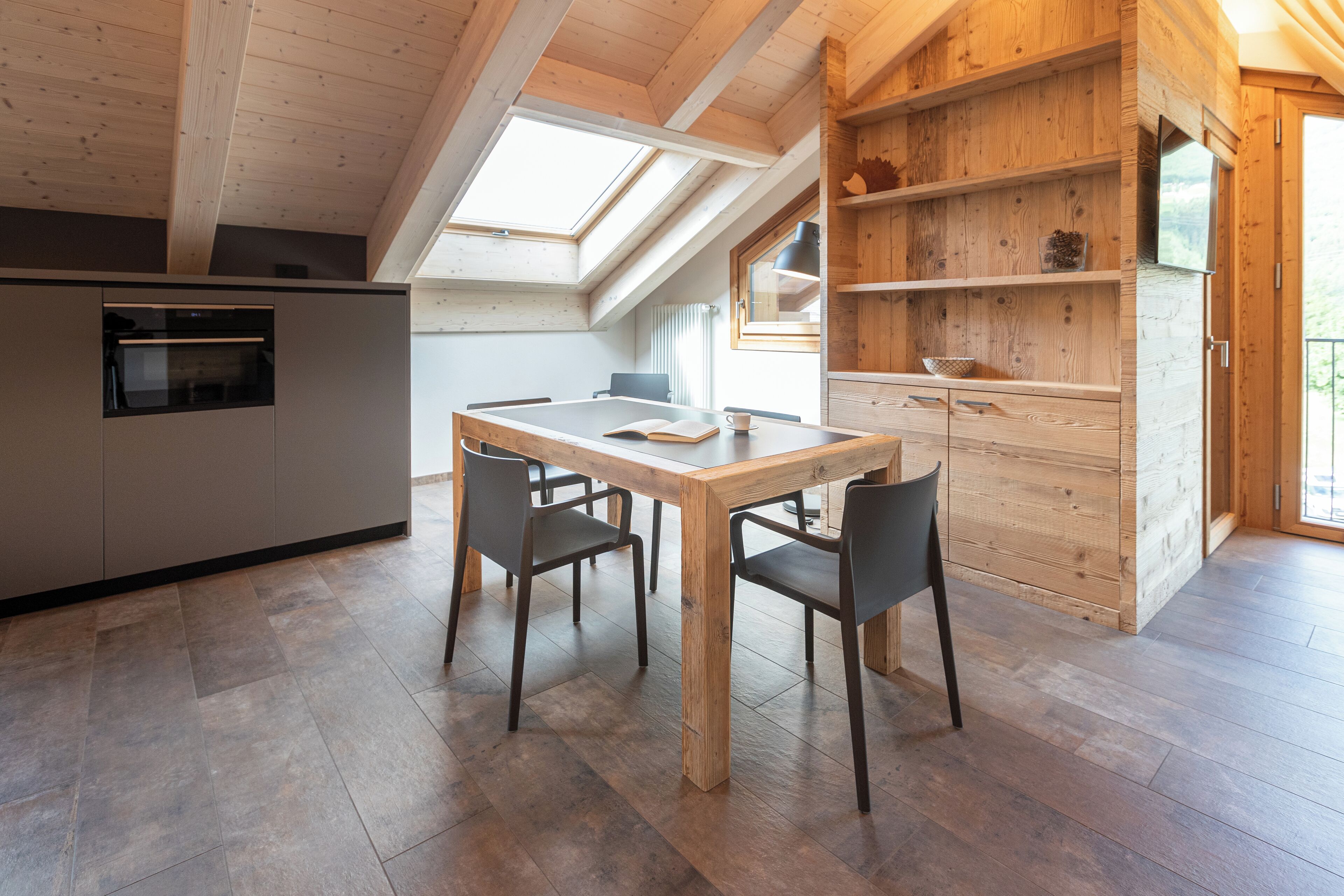 A modern kitchen with a wooden dining table and chairs, a built-in oven, and a skylight.