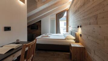 A bedroom with a wooden ceiling, a bed with white linens, a bedside table, a chair, and a TV on the wall.