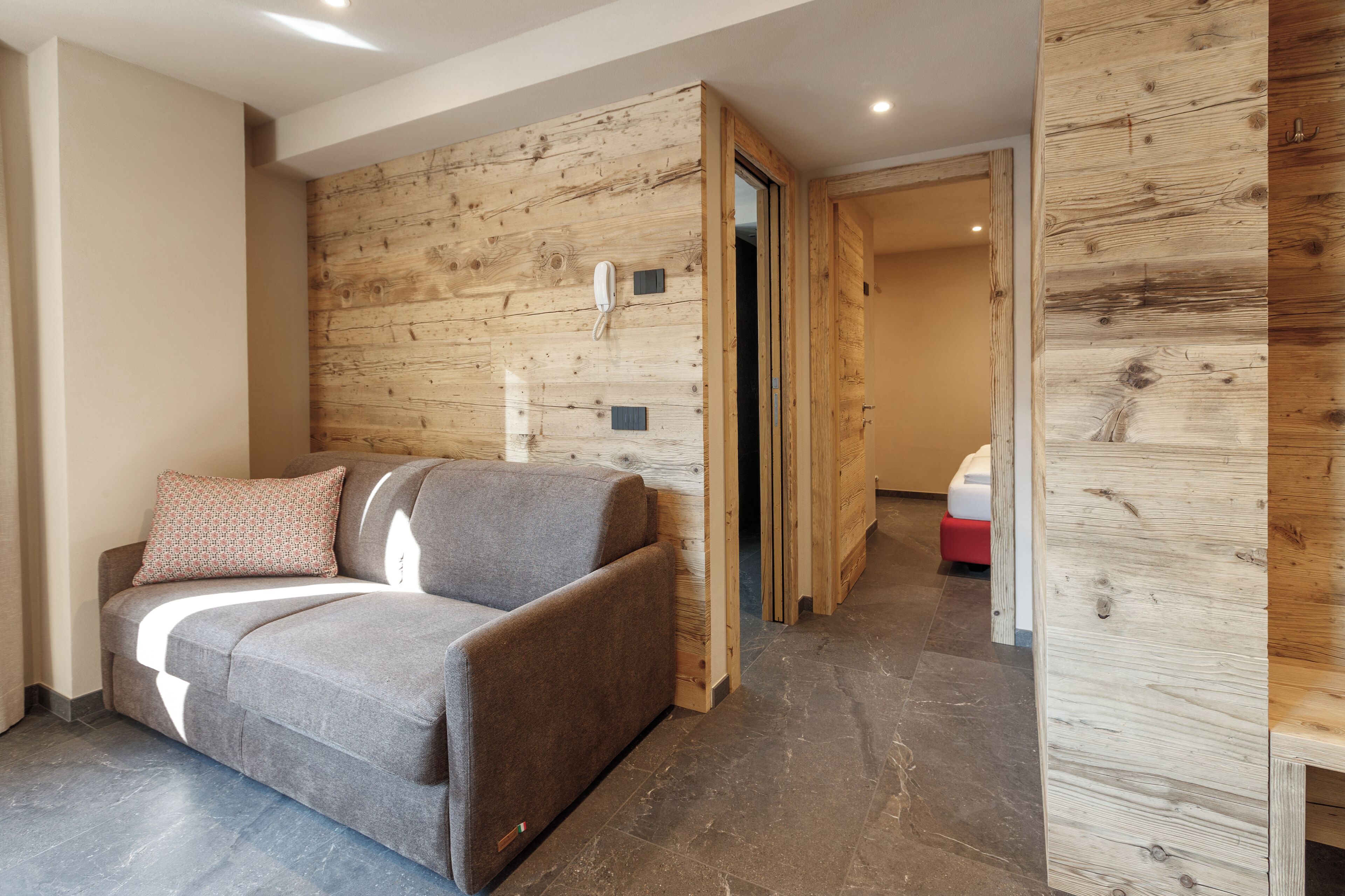 A modern living room with a grey sofa, wooden panel walls, and a tiled floor.