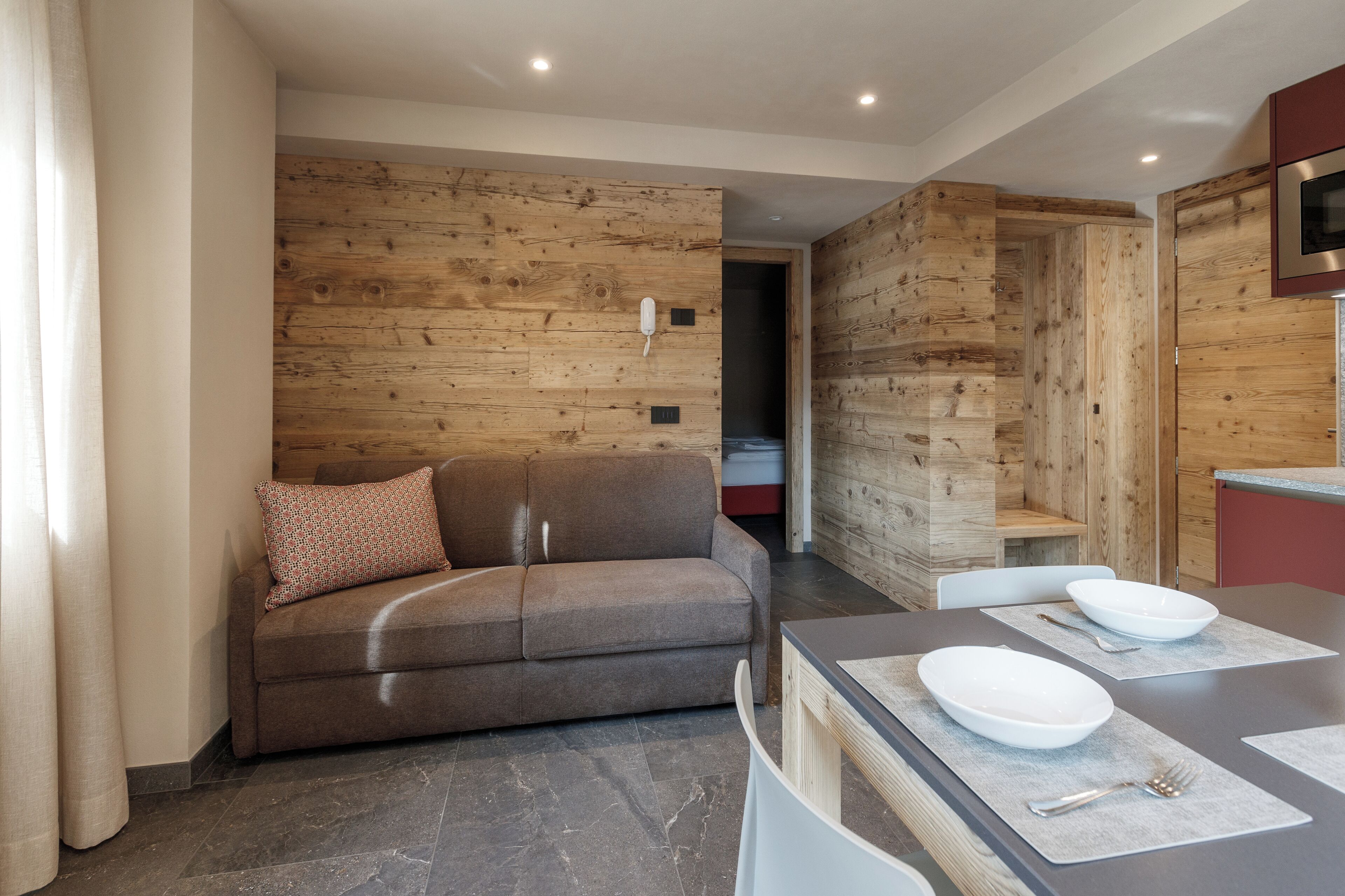 Una sala de estar moderna con un sofá marrón, una mesa de comedor con platos y cubiertos blancos, y paneles de pared de madera.