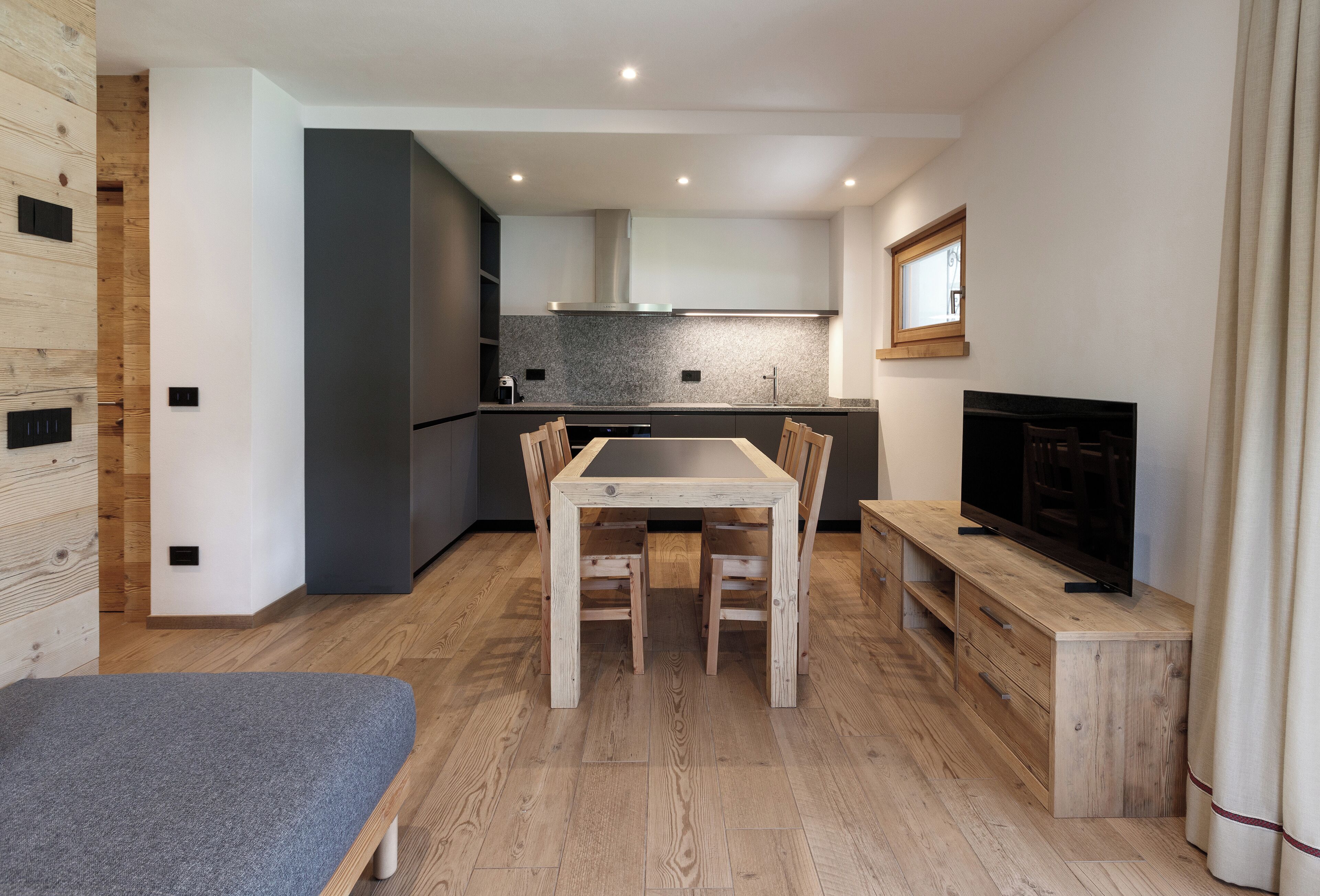 Une cuisine moderne avec un coin repas, un plancher en bois et un téléviseur posé sur un meuble en bois.