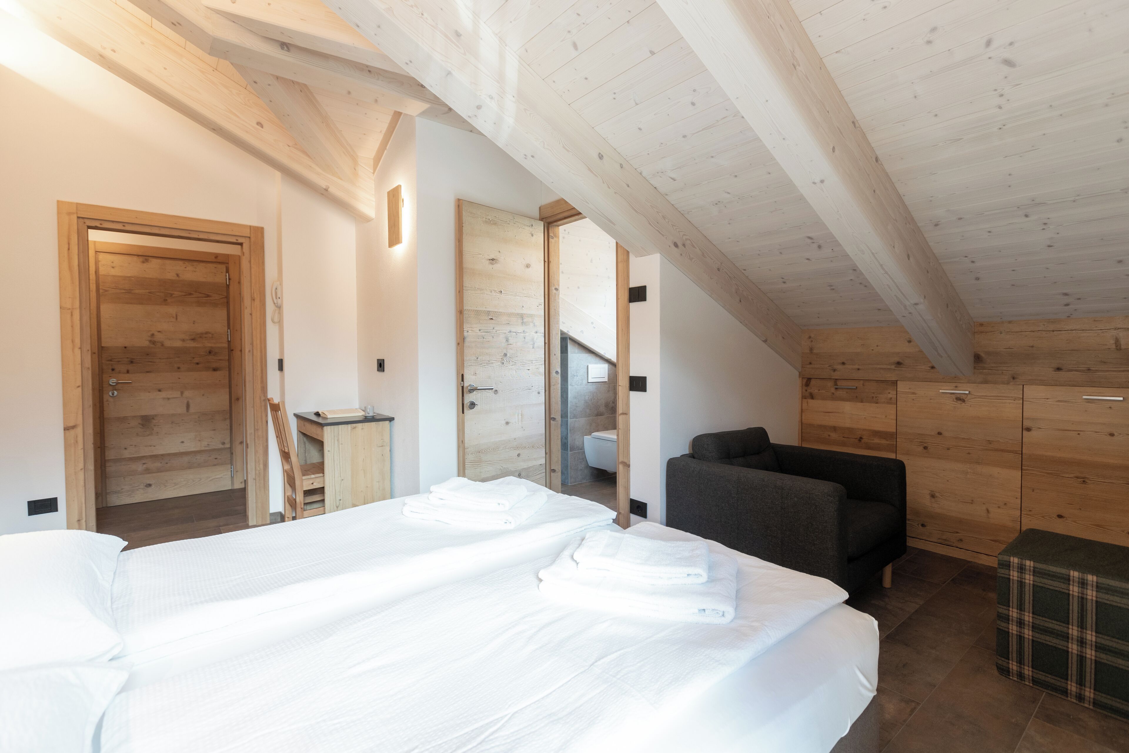 Un dormitorio con dos camas, techo de madera, un sofá y una pequeña mesa.