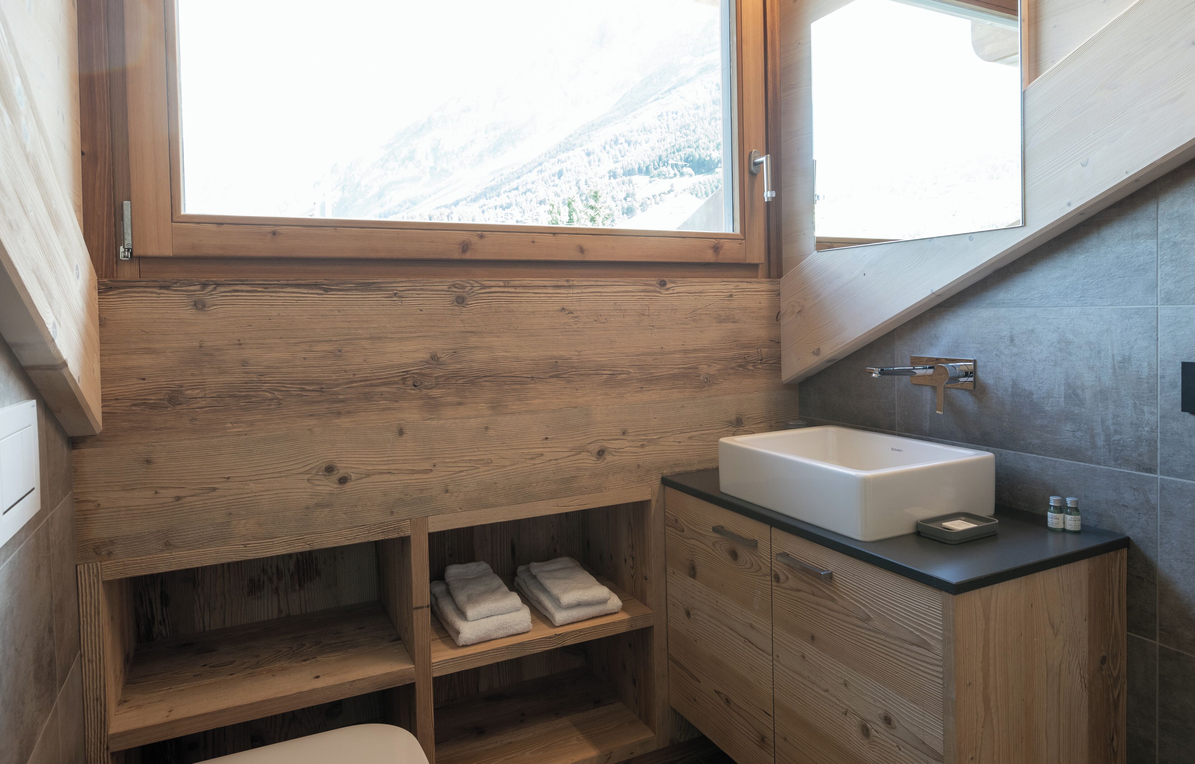 A modern bathroom with a wooden vanity, a large window, and a view of a snowy mountain.