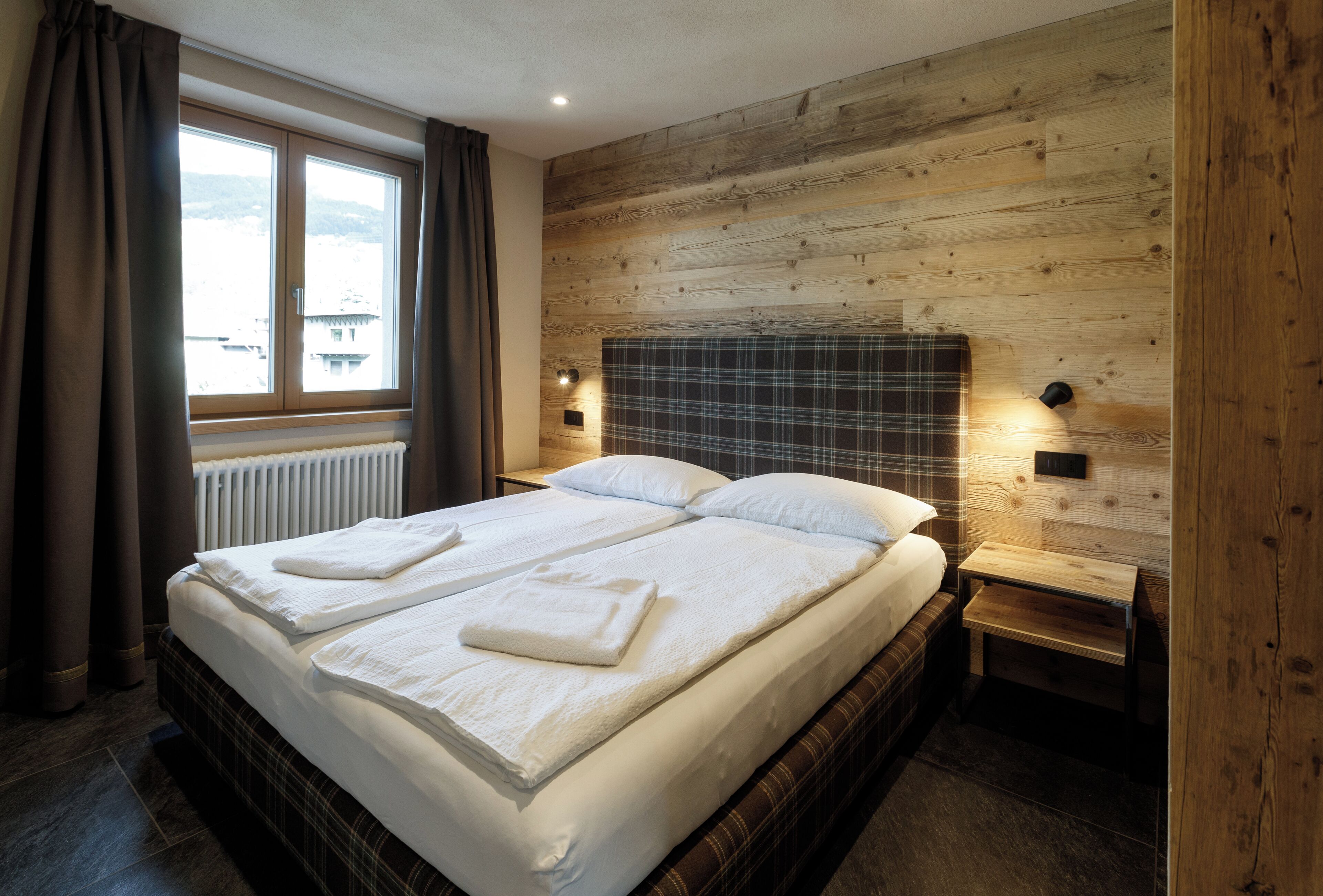 Un lit bien fait, avec du linge de lit et des serviettes blanches, une tête de lit en bois et une table de chevet avec une lampe.
