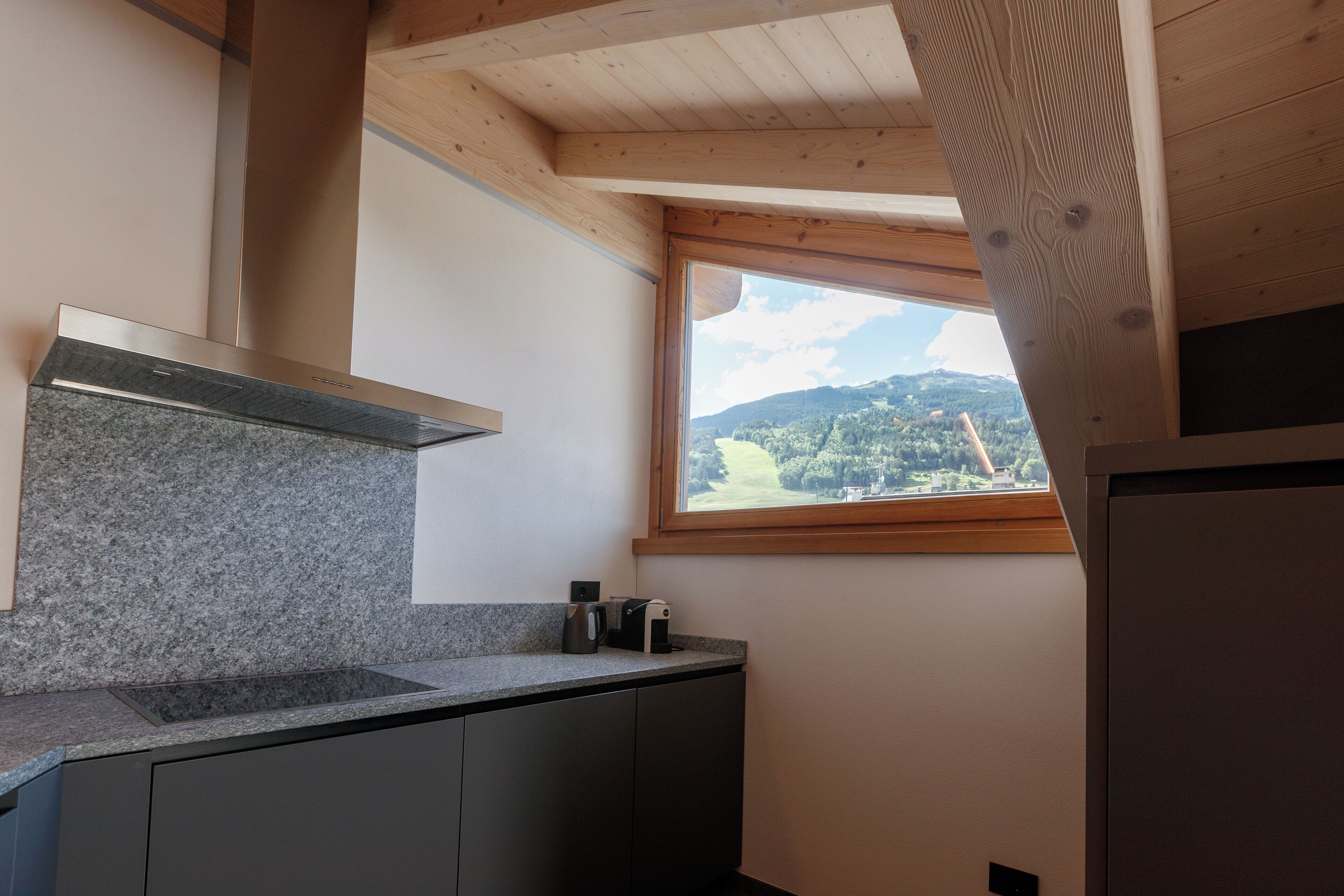 A kitchen with granite countertops, a stainless steel range hood, and a window overlooking a mountainous landscape.