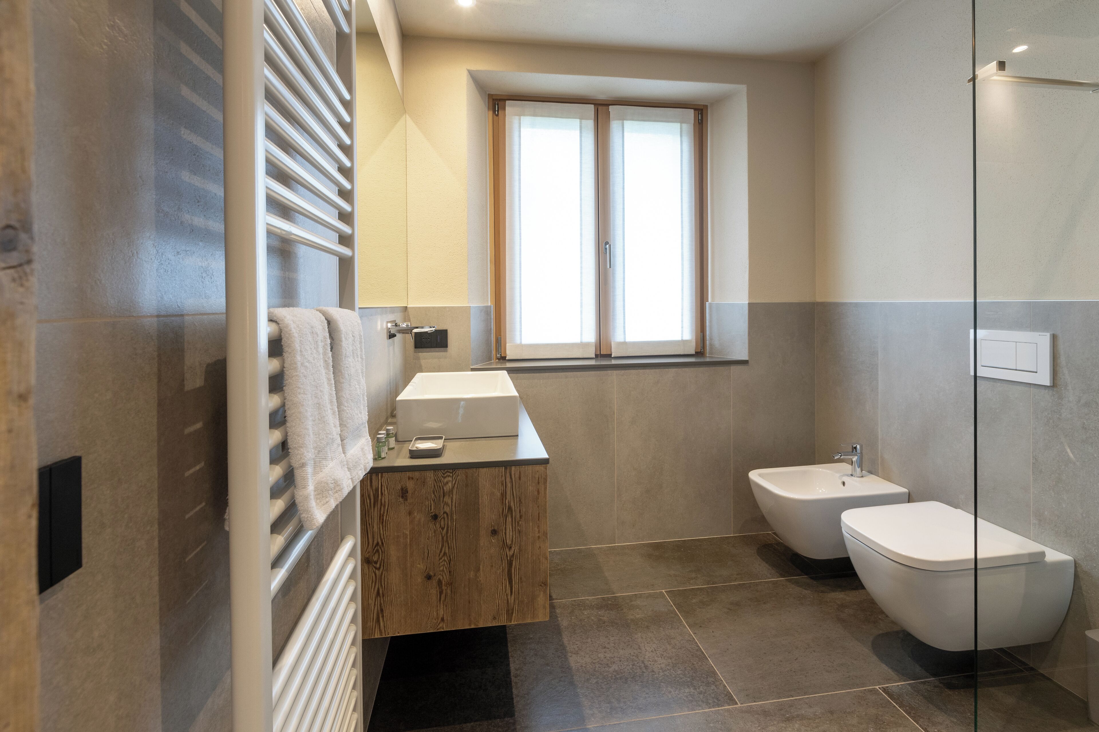A modern bathroom with a wooden vanity, a bidet, and a large window.