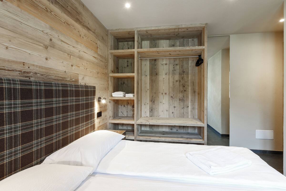 Quarto com cabeceira de madeira, cama com roupa de cama branca e estantes embutidas de madeira.