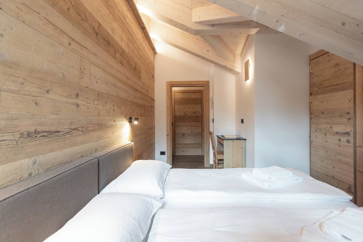 Quarto com painéis de madeira, cama com roupa de cama branca e guarda-roupa de madeira.