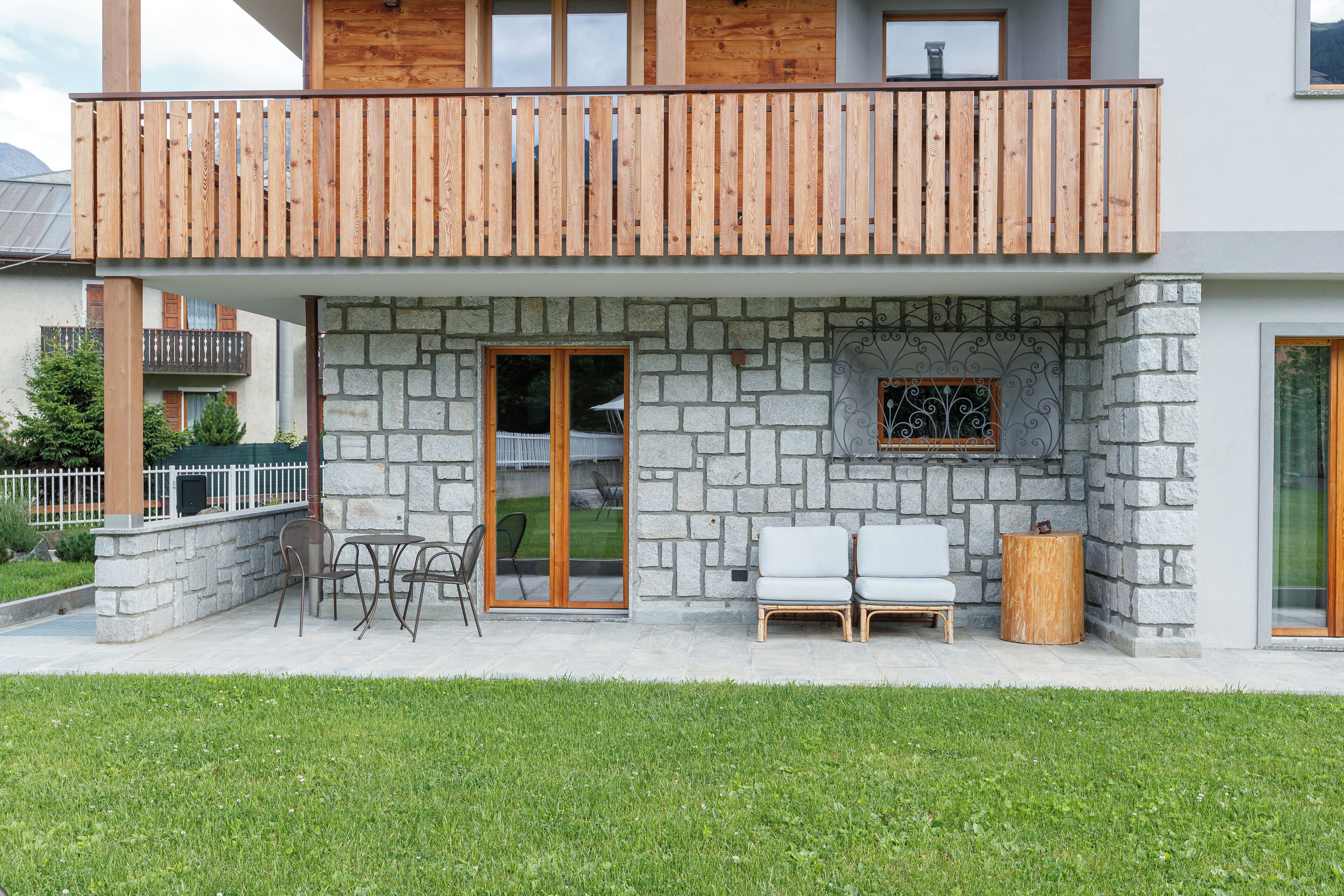 A two-story building with a stone facade, wooden balcony, and outdoor seating area.