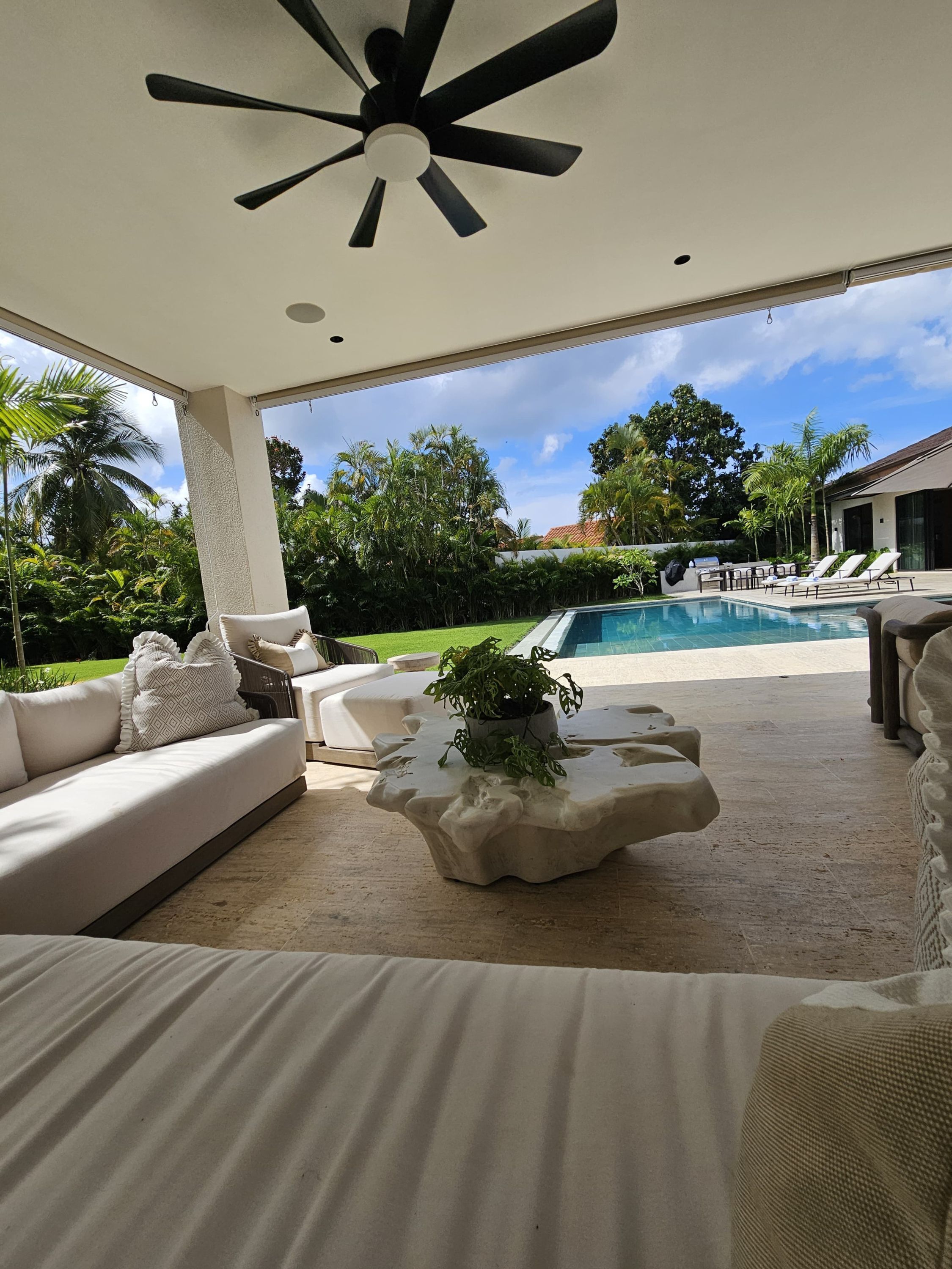A covered outdoor area with a pool, lounge chairs, and a ceiling fan.