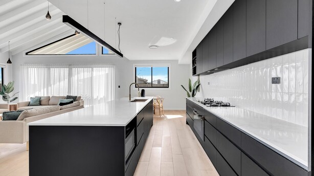 Une cuisine moderne dotée d’un îlot central, de meubles de rangement noirs et d’une grande fenêtre qui laisse entrer la lumière naturelle.