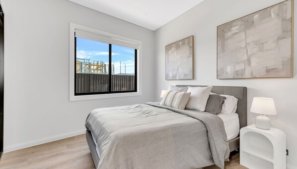 A bedroom with a large bed, a window with a view of buildings, and two abstract paintings on the wall.