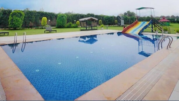 A swimming pool with a slide, surrounded by a landscaped garden and a covered seating area. -  Royal green  Spacious farmhouse with 8 bedrooms and AC, WiFi in charming Sohna (Sohna)
