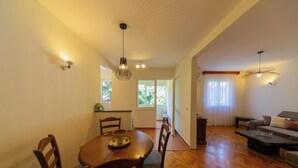 A dining area with a wooden table and chairs, a kitchen in the background, and a living room with a sofa and a coffee table. - Lovely 2 Bdr Apartment in Heart of Kotor (Dobrota)