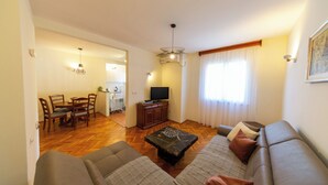 A living room with a sofa, a coffee table, and a TV. There is a dining area with a table and chairs. - Lovely 2 Bdr Apartment in Heart of Kotor (Dobrota)