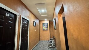 A hallway with a marble floor, wooden walls, and a ceiling with recessed lighting. There are doors on the left and a bench on the right. - Sparcles Hotel and Lounge  (Lagos)