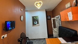A hotel lobby with a reception desk, a television, a clock, a wall-mounted plant, and a ceiling light fixture. - Sparcles Hotel and Lounge  (Lagos)